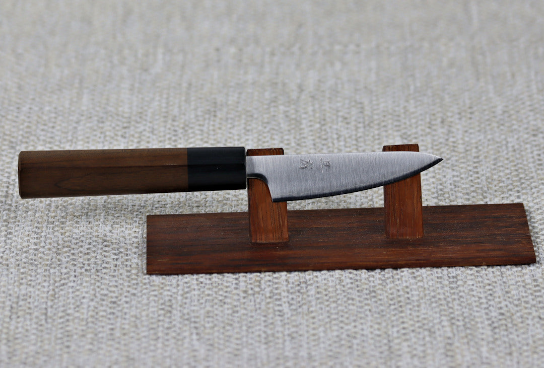 Akifusa's 80mm Paring knife in Aogami Super steel with Migaki (polished finish) on a red wood stand