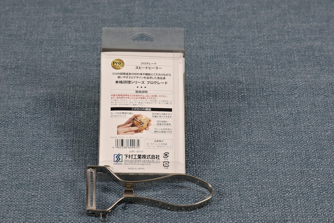 Shimomura Prograde Stainless Steel Peeler resting across the bottom of the backside of packaging peeler bottom side up