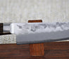 Ohishi Ginsan 135mm Petty (Utility) Japanese Kitchen knife on the red wood stand close up of the engraving near the integral bolster and the pear skin finish