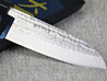 Ohishi SLD 165mm Santoku(General Purpose) Japanese Kitchen Knife close up of the blade and it polished/hammered finish resting at an angle across its packaging