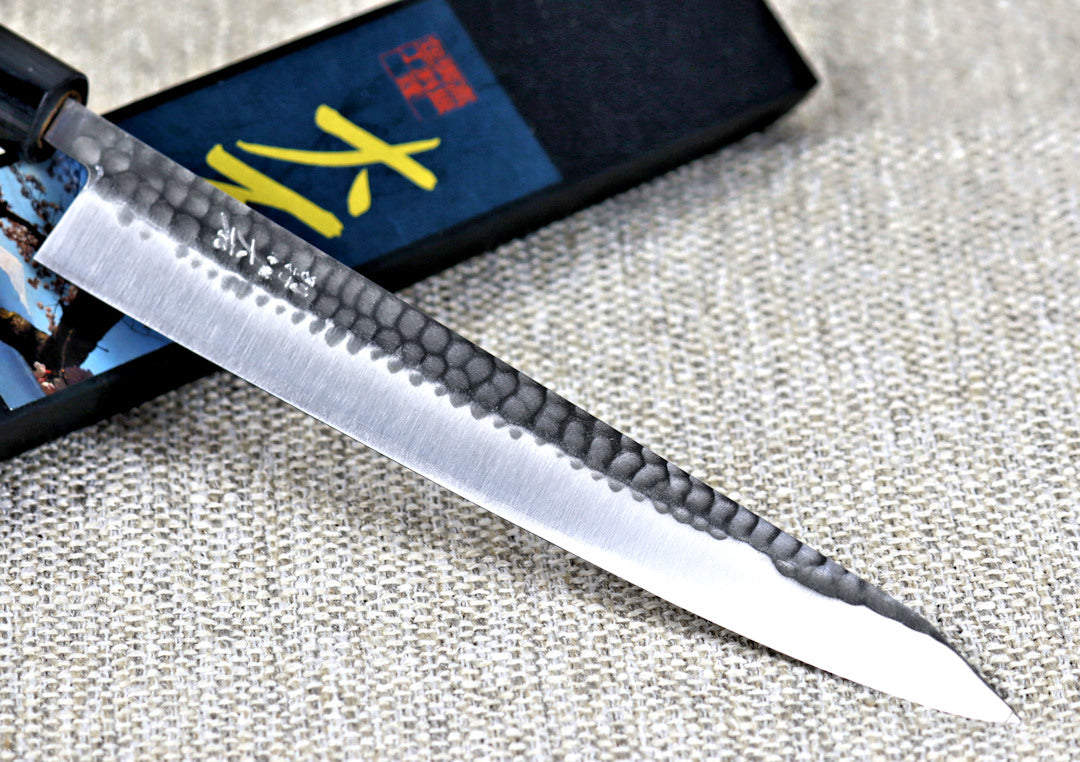 Ohishi SLD Migaki/Tsuchime Sujihiki (Slicer) Japanese Kitchen Knife close up of blade and engraving resting across its packaging