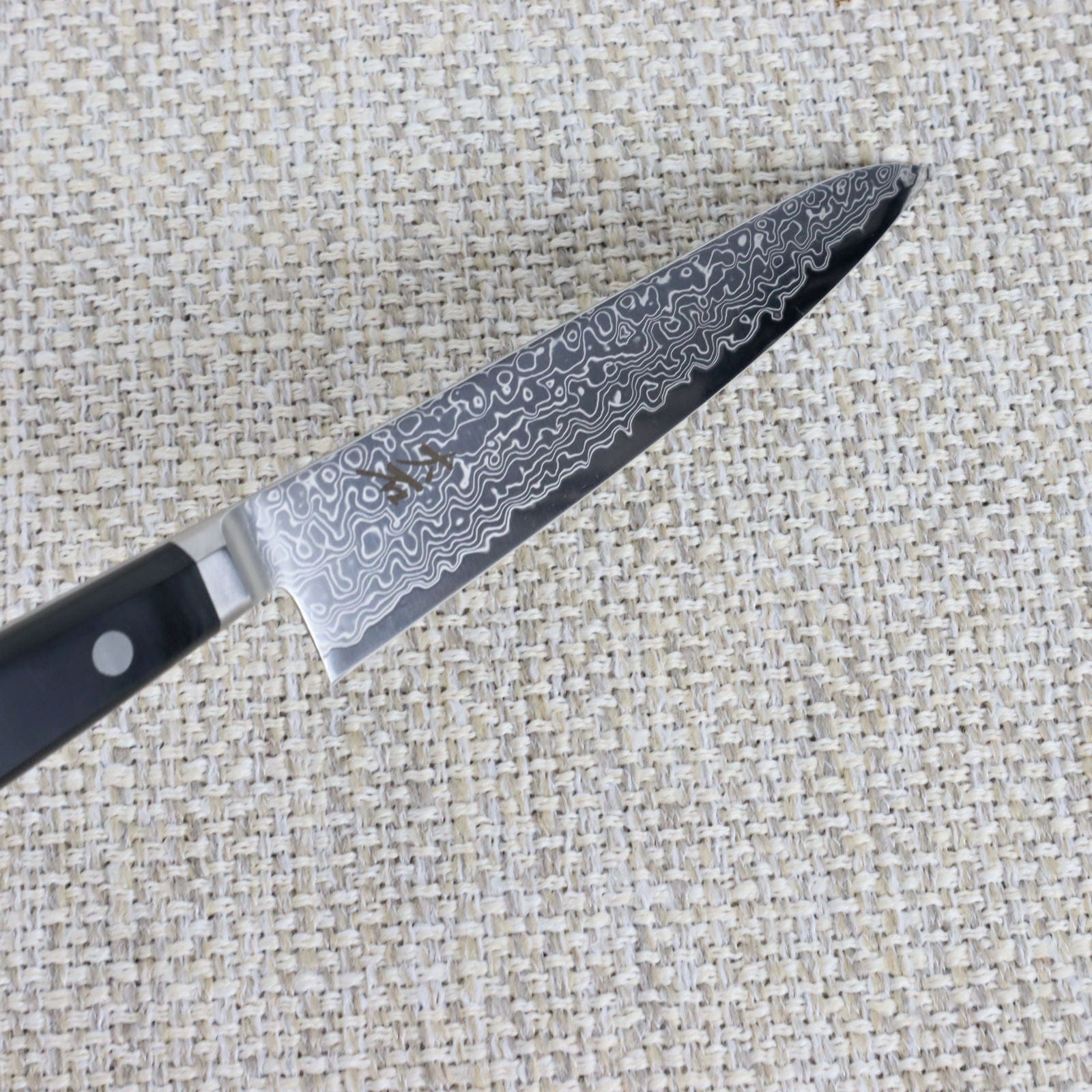Ohishi Classic Powder Metal Damascus 150mm Petty (Utility) Japanese kitchen knife with the blade angled down to show the integral bolster and the Damascus blade