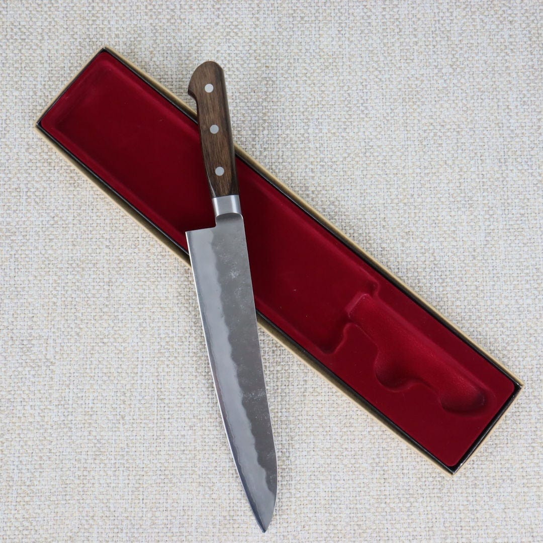 Ohishi Ginsan 240mm Gyuto (Chef/Cook) Japanese Kitchen Knife resting at an angle across its red packaging insert.